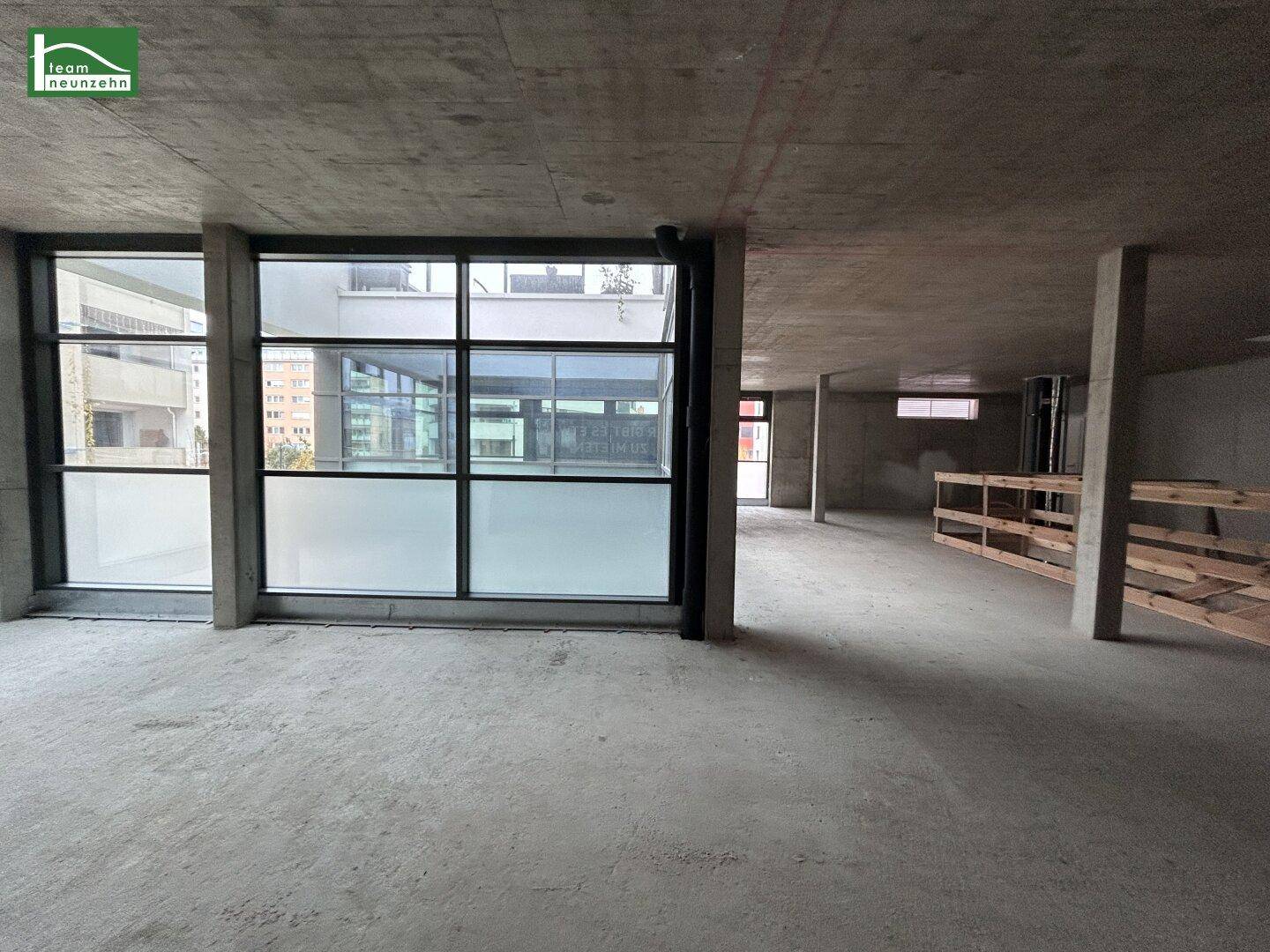 Großer Gewerberaum im Rohbau mit Betonoberflächen, großen Fenstern und Holzkonstruktionen.