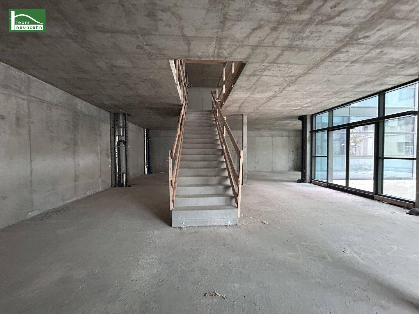 Großer, unfertiger Gewerberaum mit Betontreppe, hohen Decken und großen Fenstern.