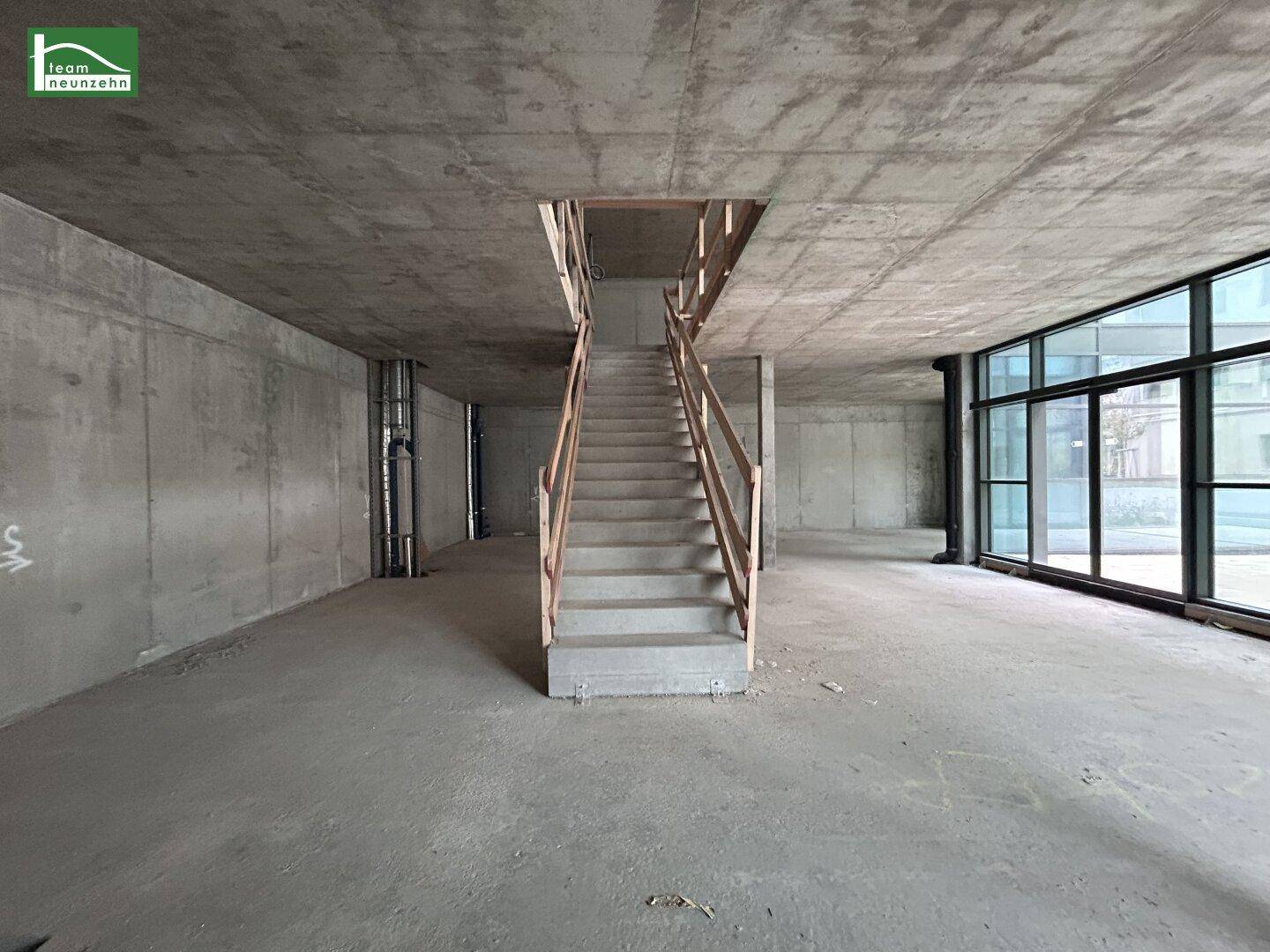 Großer, unfertiger Gewerberaum mit Betontreppe, hohen Decken und großen Fenstern.