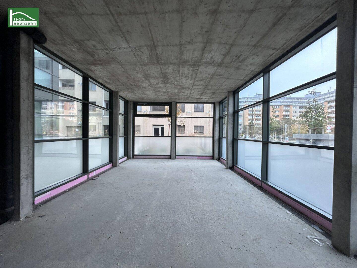 Unfertiger Gewerberaum mit großen Fenstern, Betonboden und -decke, bereit für den Ausbau.