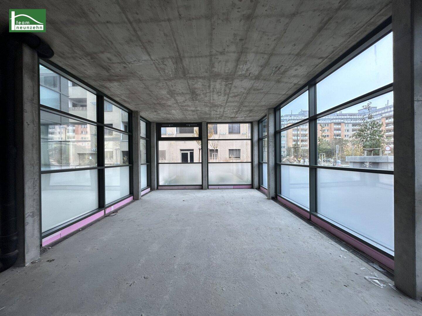 Unfertiger Gewerberaum mit großen Fenstern, Betonboden und -decke, bereit für den Ausbau.