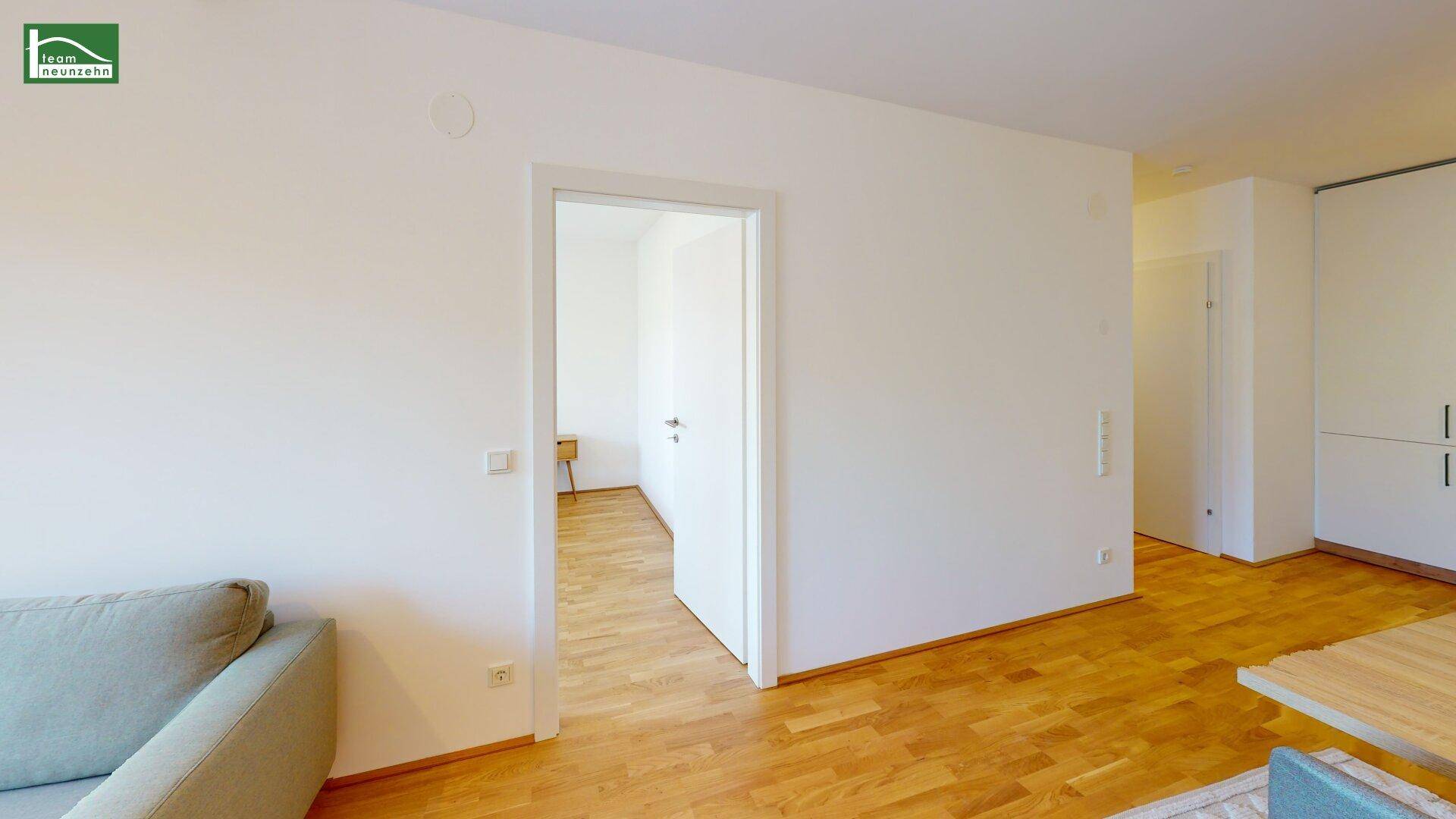 Heller Wohnbereich mit Parkettboden, weißen Wänden und offenem Zugang zu einem weiteren Zimmer.
