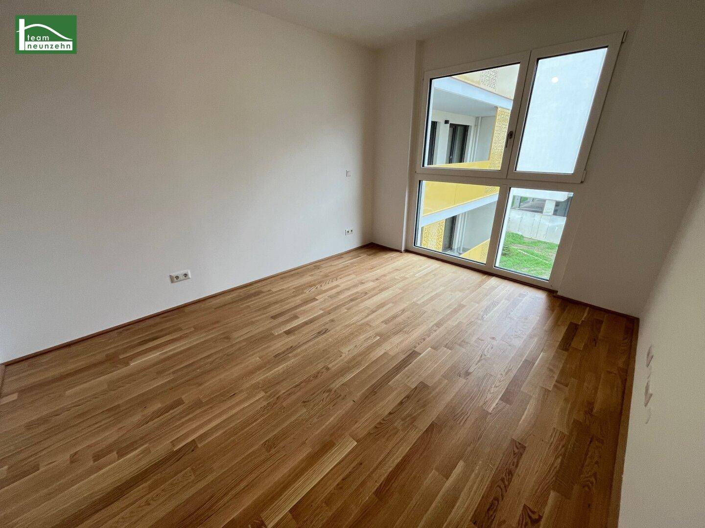 Schlafzimmer mit großen Fenstern und Parkettboden, bietet einen Blick auf die umliegenden Gebäude.