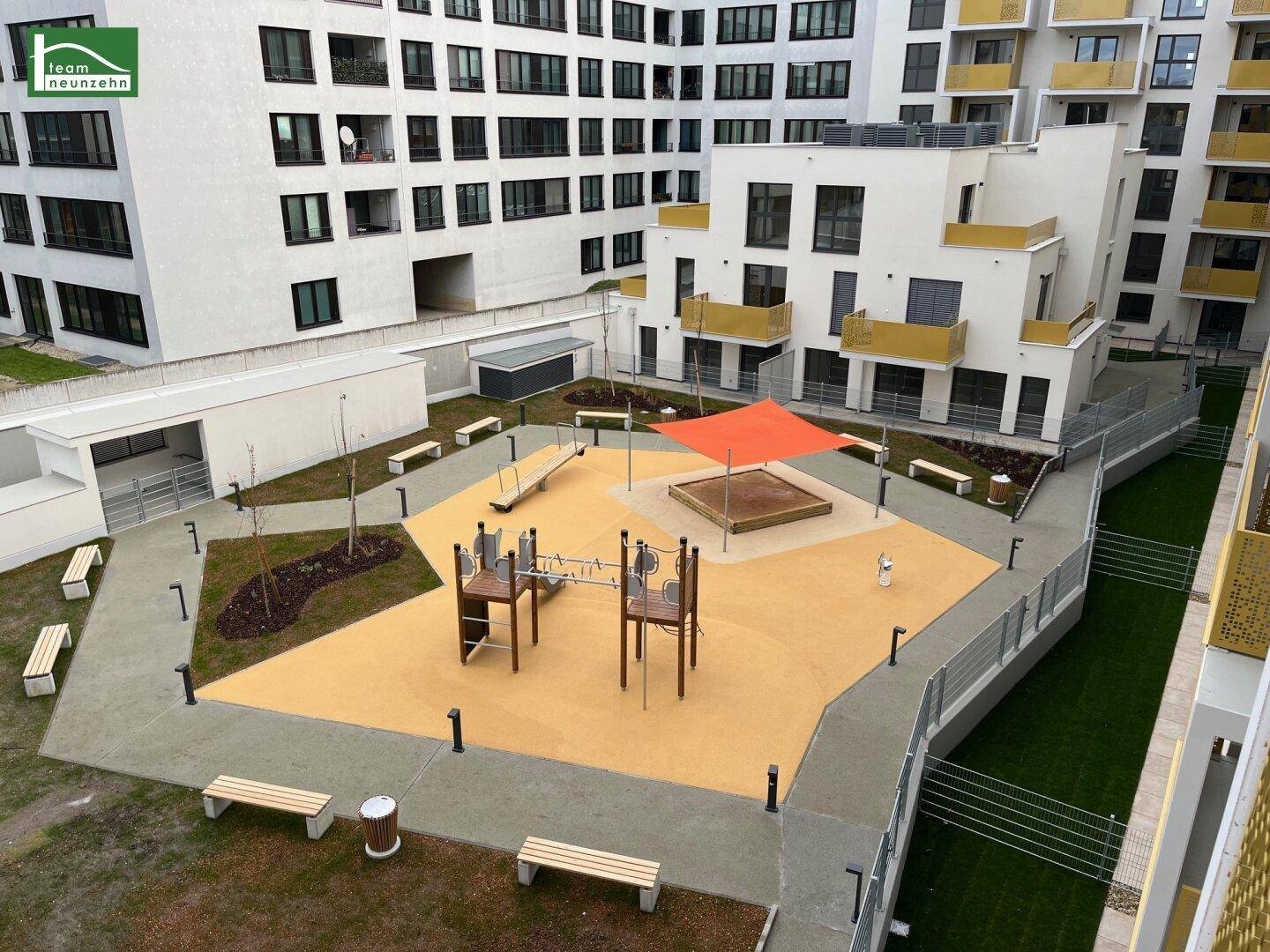 Moderner Kinderspielplatz im Innenhof der Wohnanlage mit verschiedenen Spielgeräten und Sitzbänken.