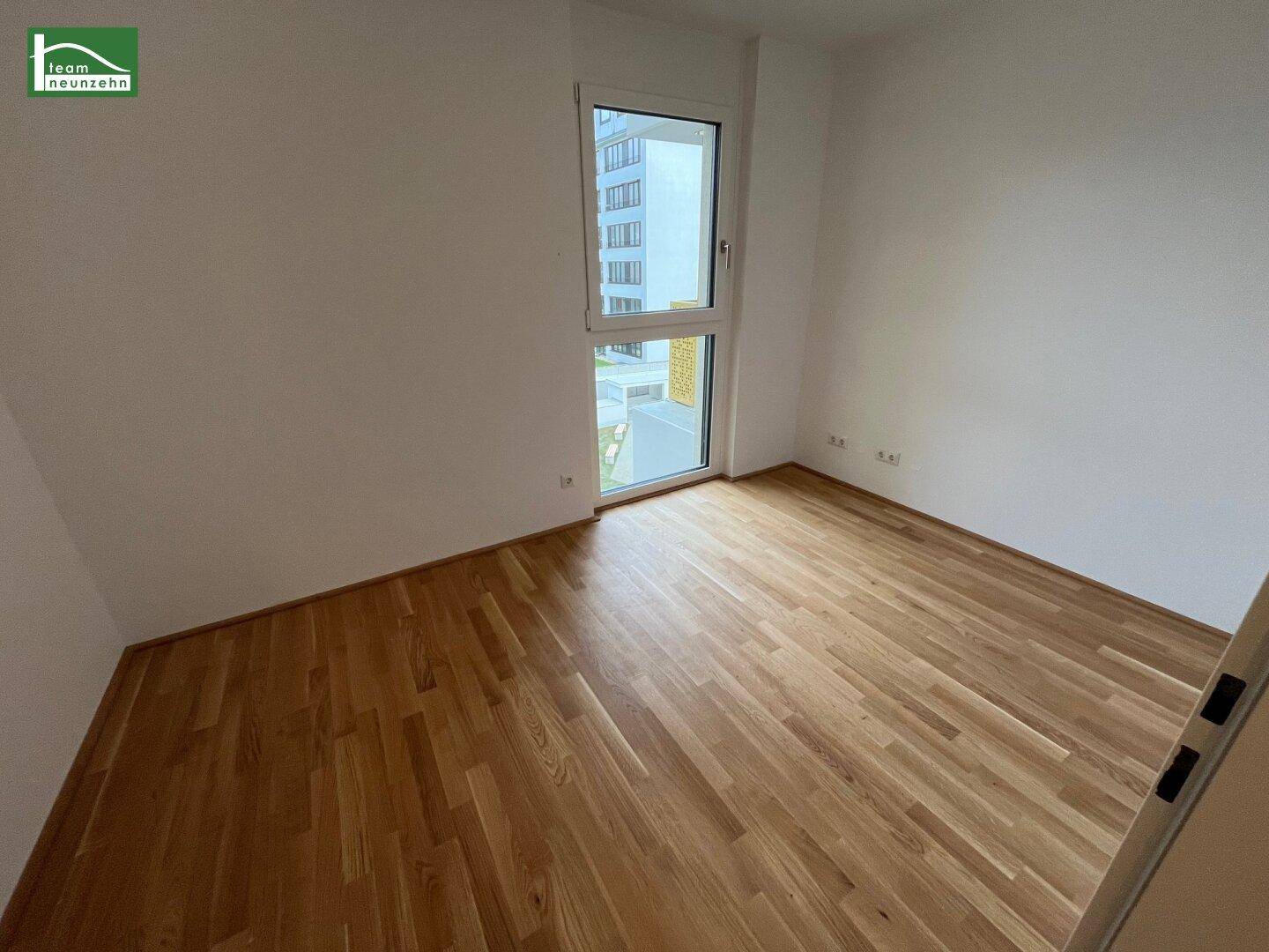 Helles Schlafzimmer mit Parkettboden und einem großen Fenster, das viel natürliches Licht spendet.