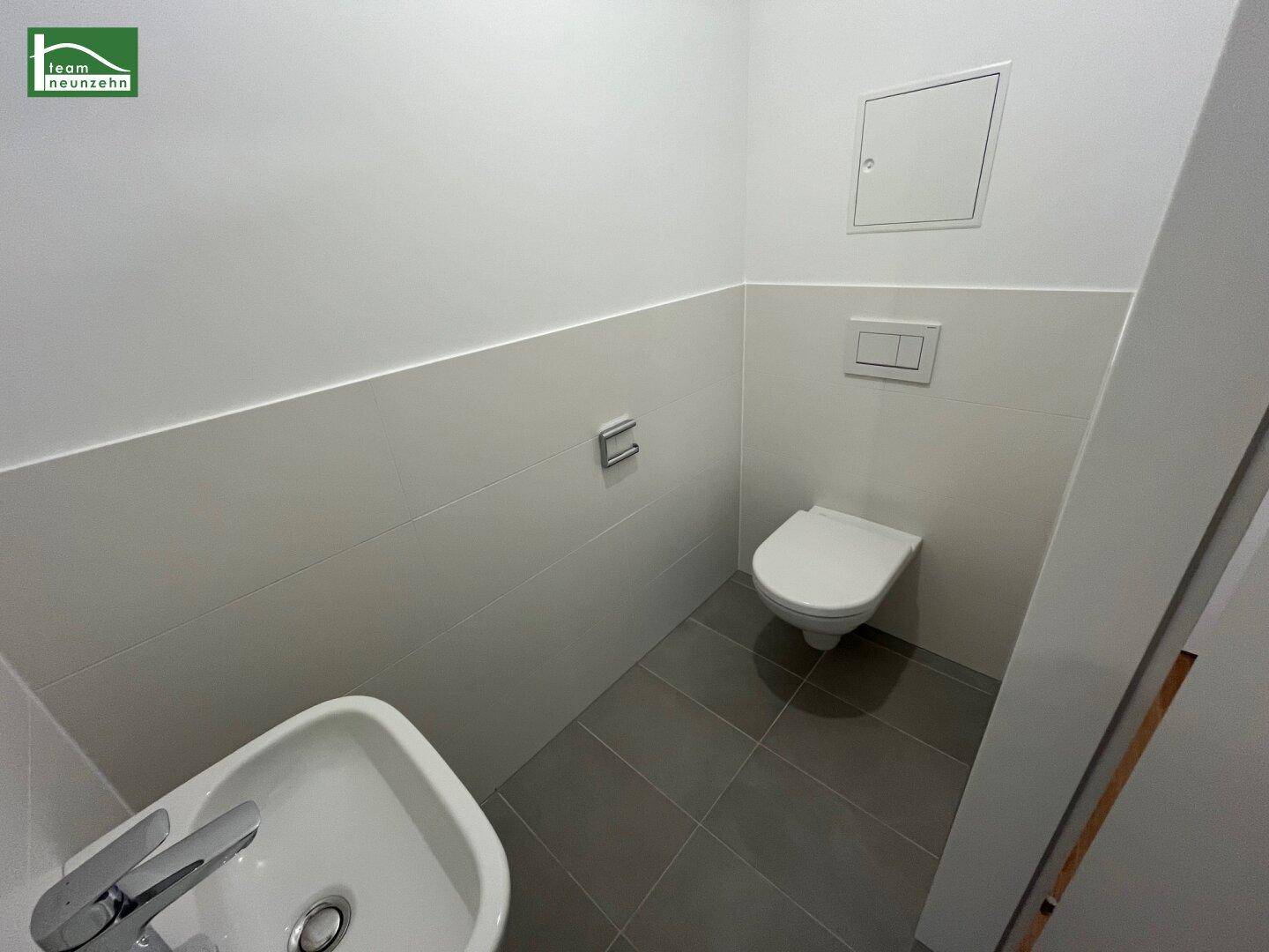 Separate Gästetoilette mit Wand-WC und kleinem Waschbecken, ausgestattet mit modernen Fliesen.