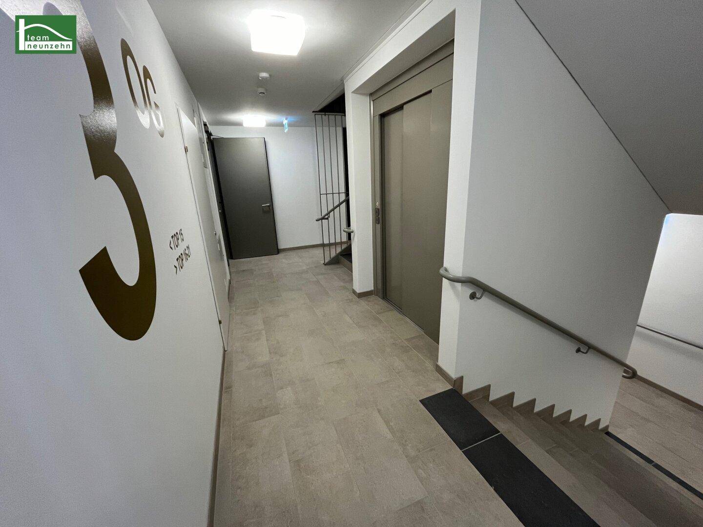 Heller Flur im Gebäude mit Aufzug und Treppenhaus, der zu den einzelnen Wohneinheiten führt.