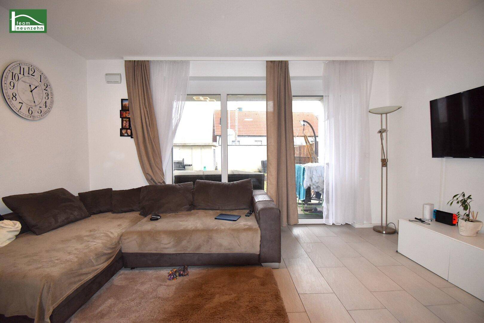 Gemütliches Wohnzimmer mit großem Ecksofa, Fernseher und Zugang zu einem Außenbereich.