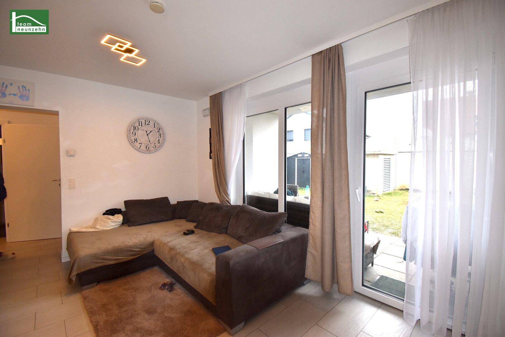 Heller Wohnbereich mit beigem Ecksofa und direktem Zugang zum Garten durch große Fenster.