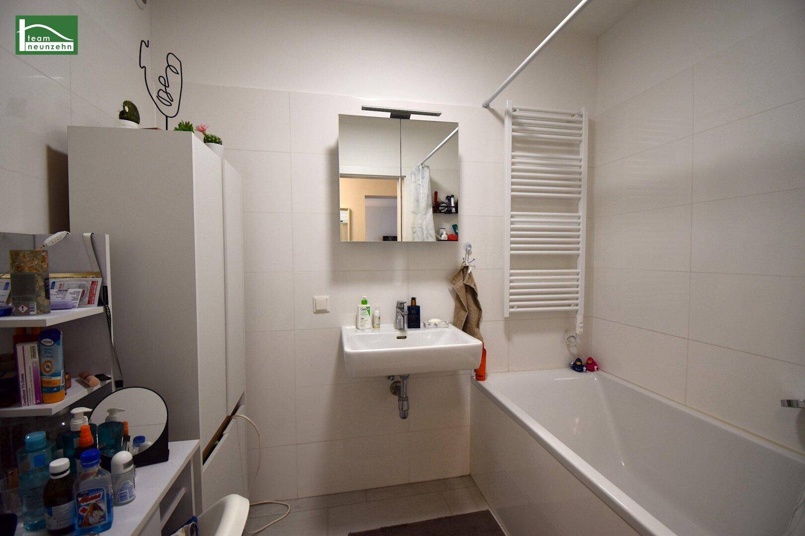Modernes Badezimmer mit Badewanne, Waschbecken, Spiegelschrank und Handtuchheizkörper.