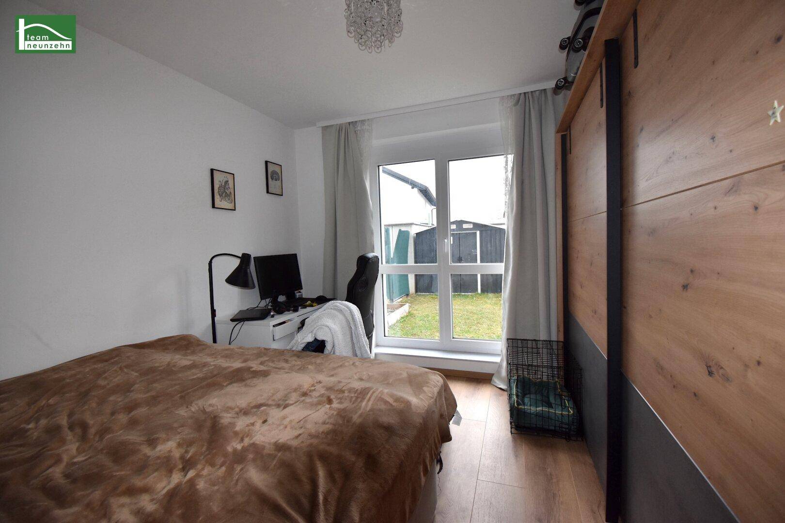 Schlafzimmer mit Holzboden, Arbeitsbereich und Blick auf den Garten durch ein großes Fenster.