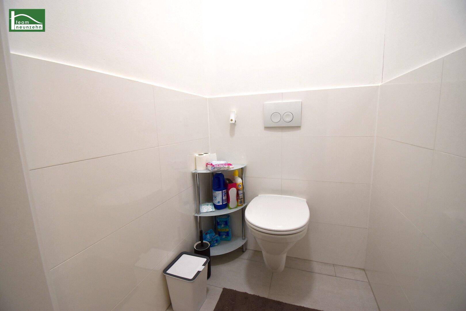 Separates WC mit wandhängender Toilette und hellen Fliesen an Wänden und Boden.
