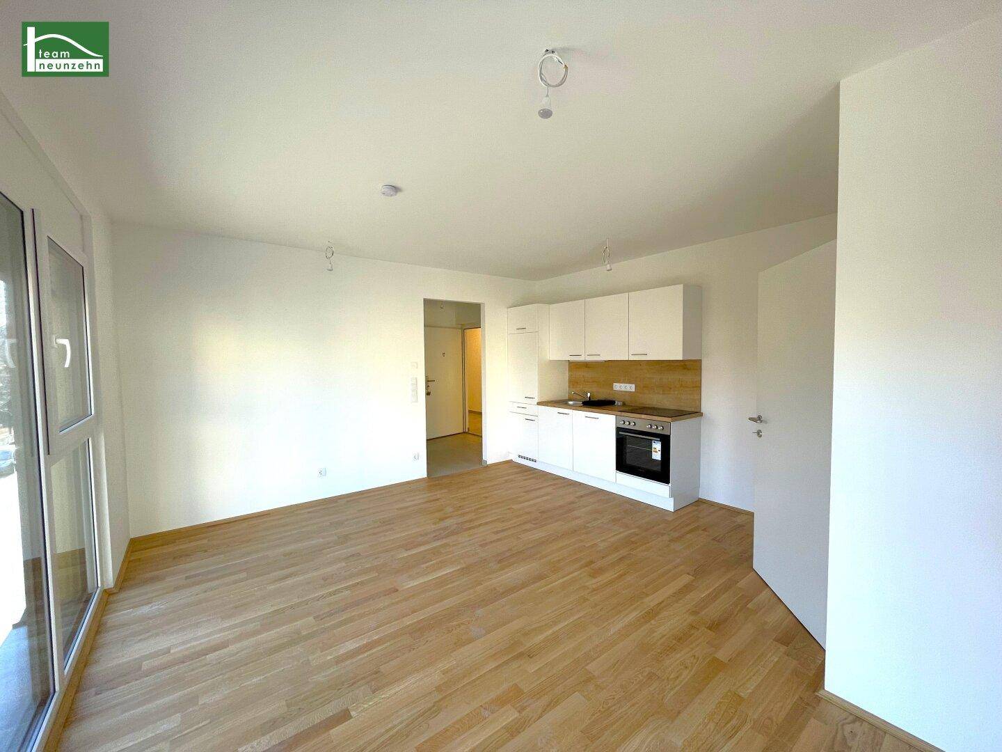 Heller Wohn-Essbereich mit integrierter Küchenzeile, Parkettboden und Zugang zu einem Balkon.