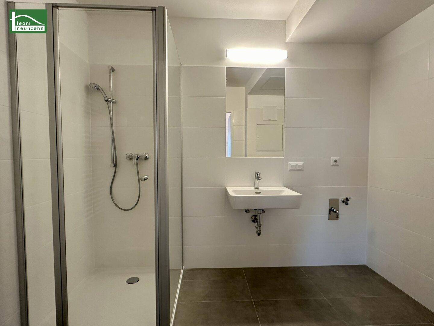Modernes Badezimmer mit ebenerdiger Dusche, Waschbecken und großen weißen Fliesen.