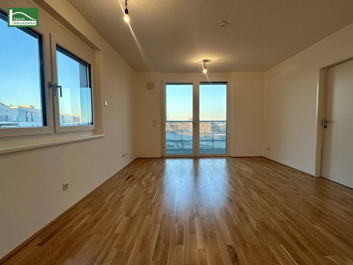 Geräumiges, leeres Wohnzimmer mit Holzboden und großen Fenstern für viel Tageslicht.