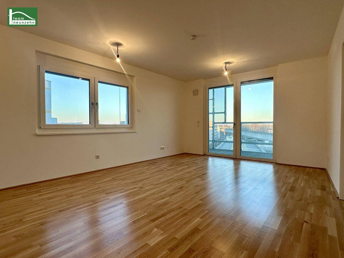 Helles, leeres Wohnzimmer mit Parkettboden und Zugang zu einem Balkon, gut beleuchtet.