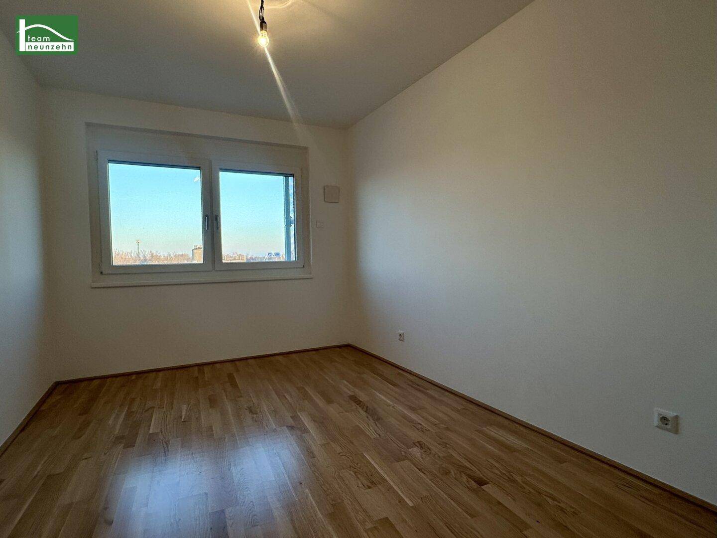 Helles, leeres Zimmer mit Parkettboden und großem Fenster, ideal als Schlafzimmer nutzbar.