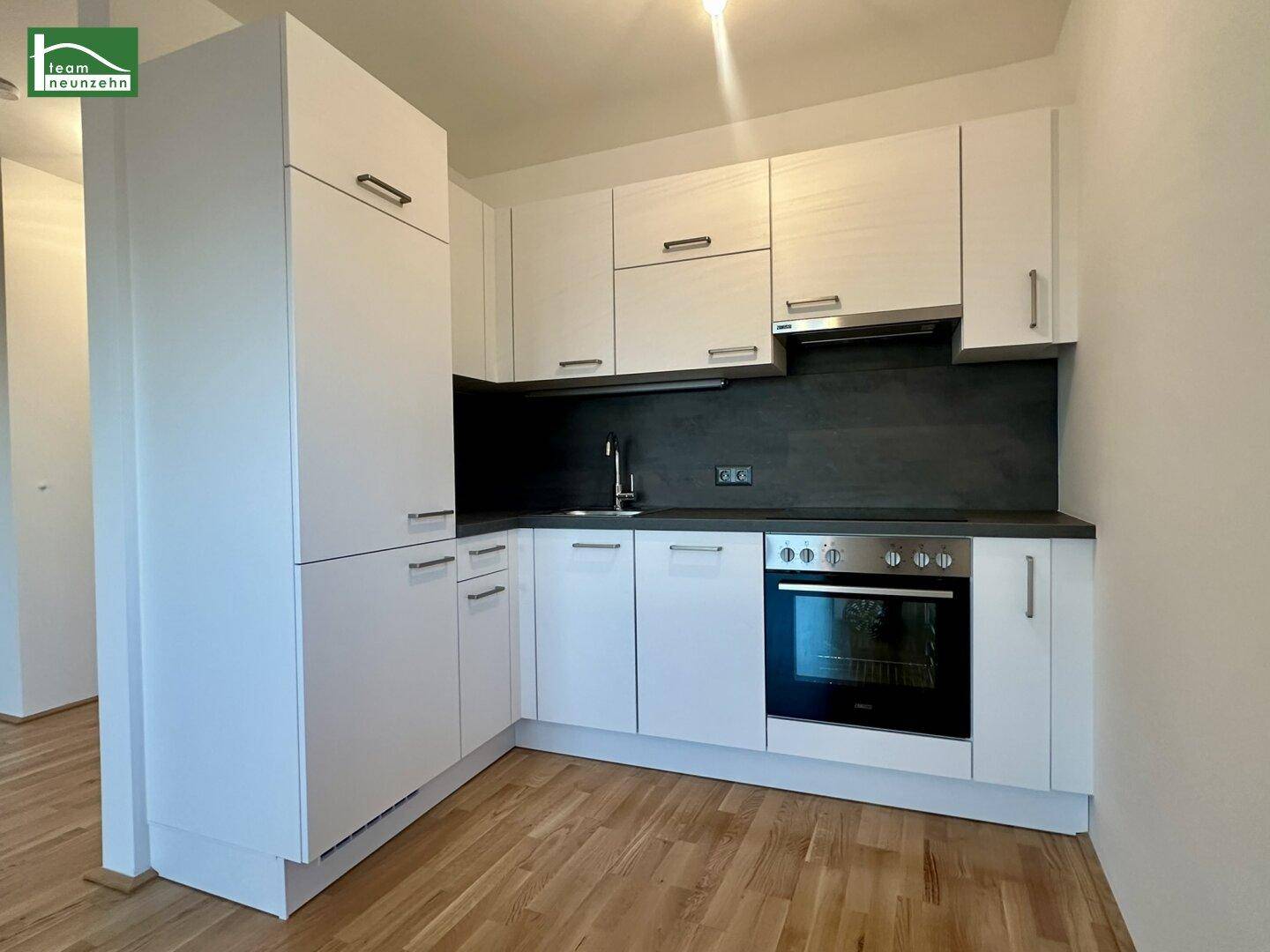 Moderne Einbauküche mit weißen Schränken, dunkler Arbeitsplatte und integriertem Backofen.