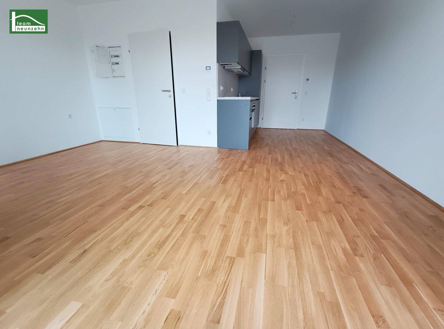 Leerer Raum mit hellem Holzfußboden und einer modernen grauen Küchenzeile, bereit zur individuellen Gestaltung.