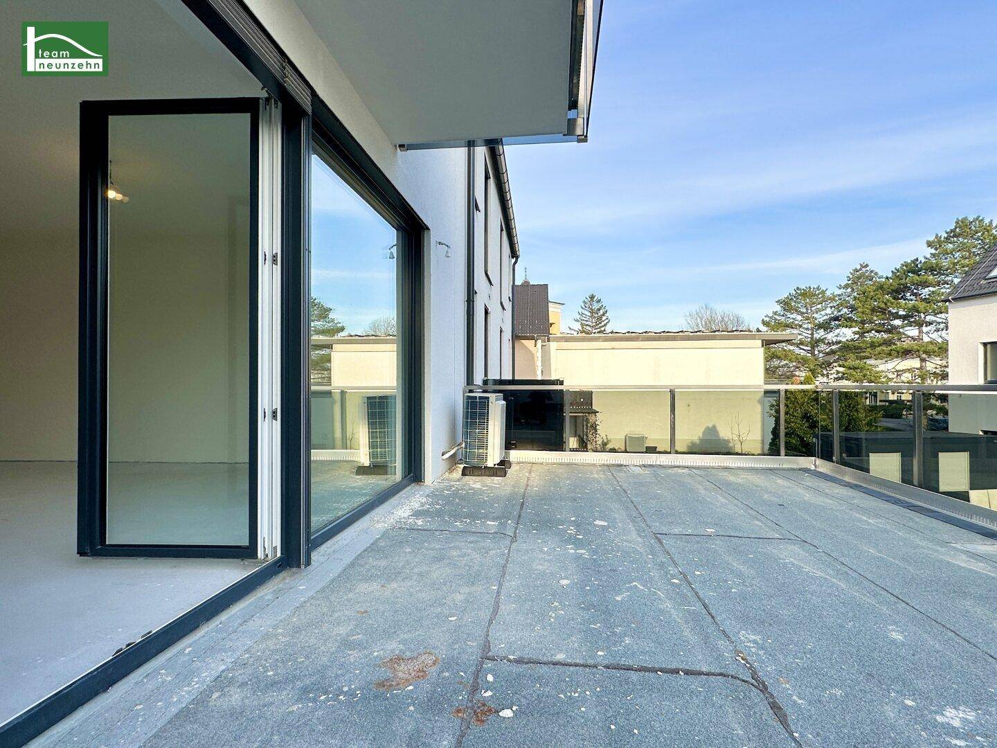 Große Dachterrasse mit weitem Blick und einer Klimaanlage, zugänglich durch breite Glastüren.
