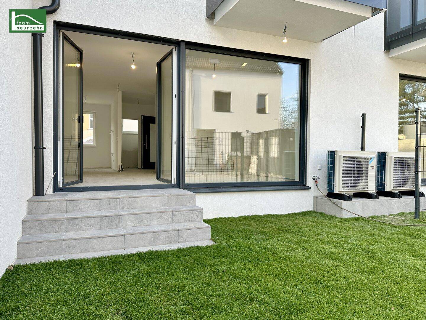 Kleiner Gartenbereich mit Rasenfläche und Zugang zu einem hellen Innenraum durch große Glastüren.