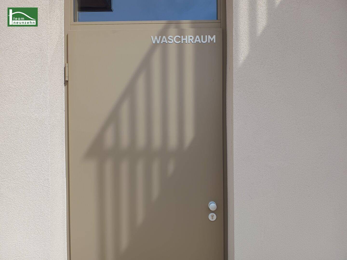 Eingang zum Waschraum mit brauner Tür und kleinem Fenster, außen am Gebäude gelegen.