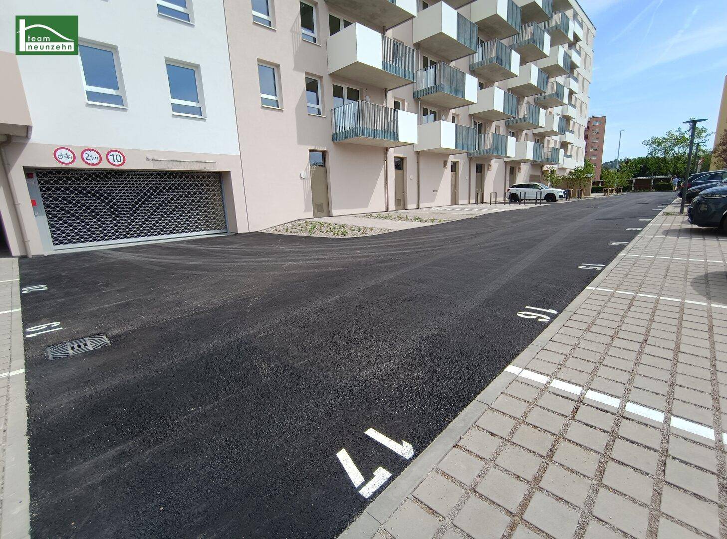 Außenparkplätze vor einem modernen Wohngebäude mit Tiefgaragenzufahrt und Balkonen.