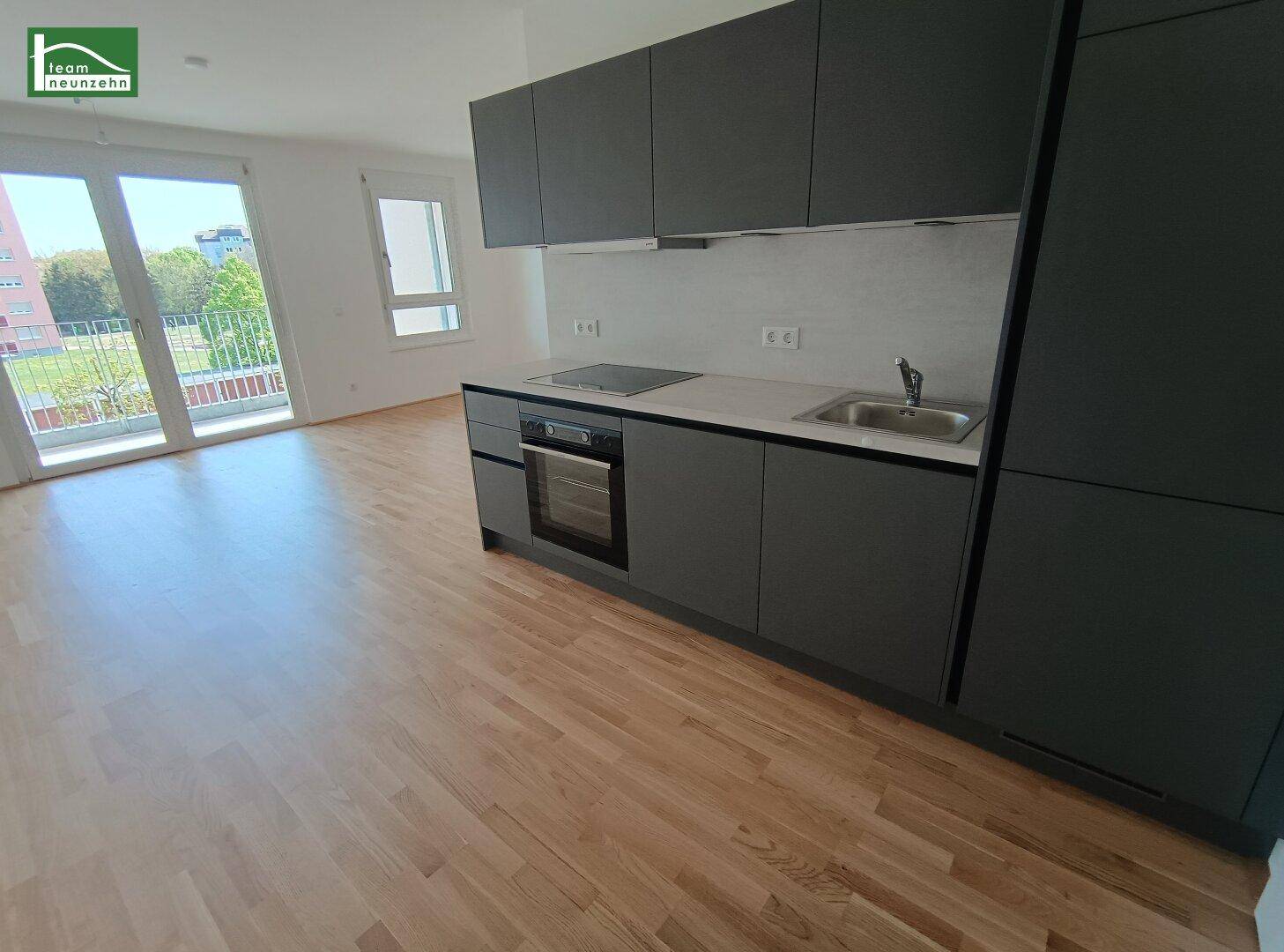 Moderne Einbauküche in Grau mit integriertem Backofen und hellem Holzfußboden, mit Zugang zum Balkon.