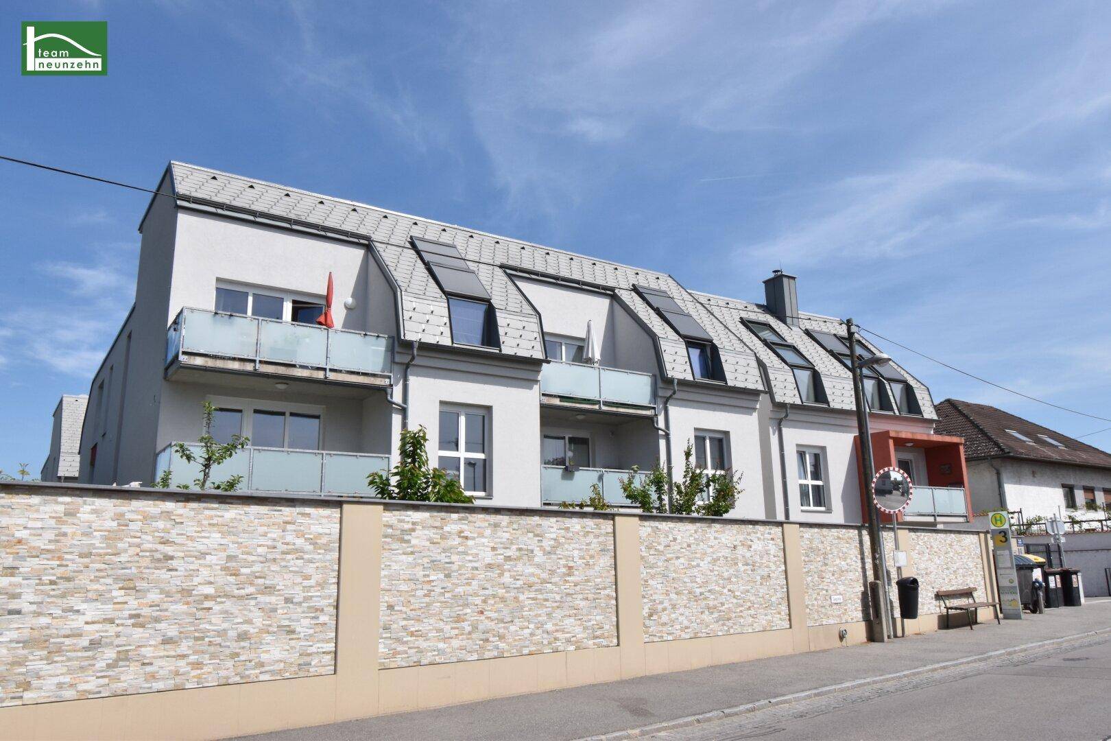 Ansicht eines modernen Wohngebäudes mit Balkonen und einer dekorativen Steinmauer im Vordergrund.
