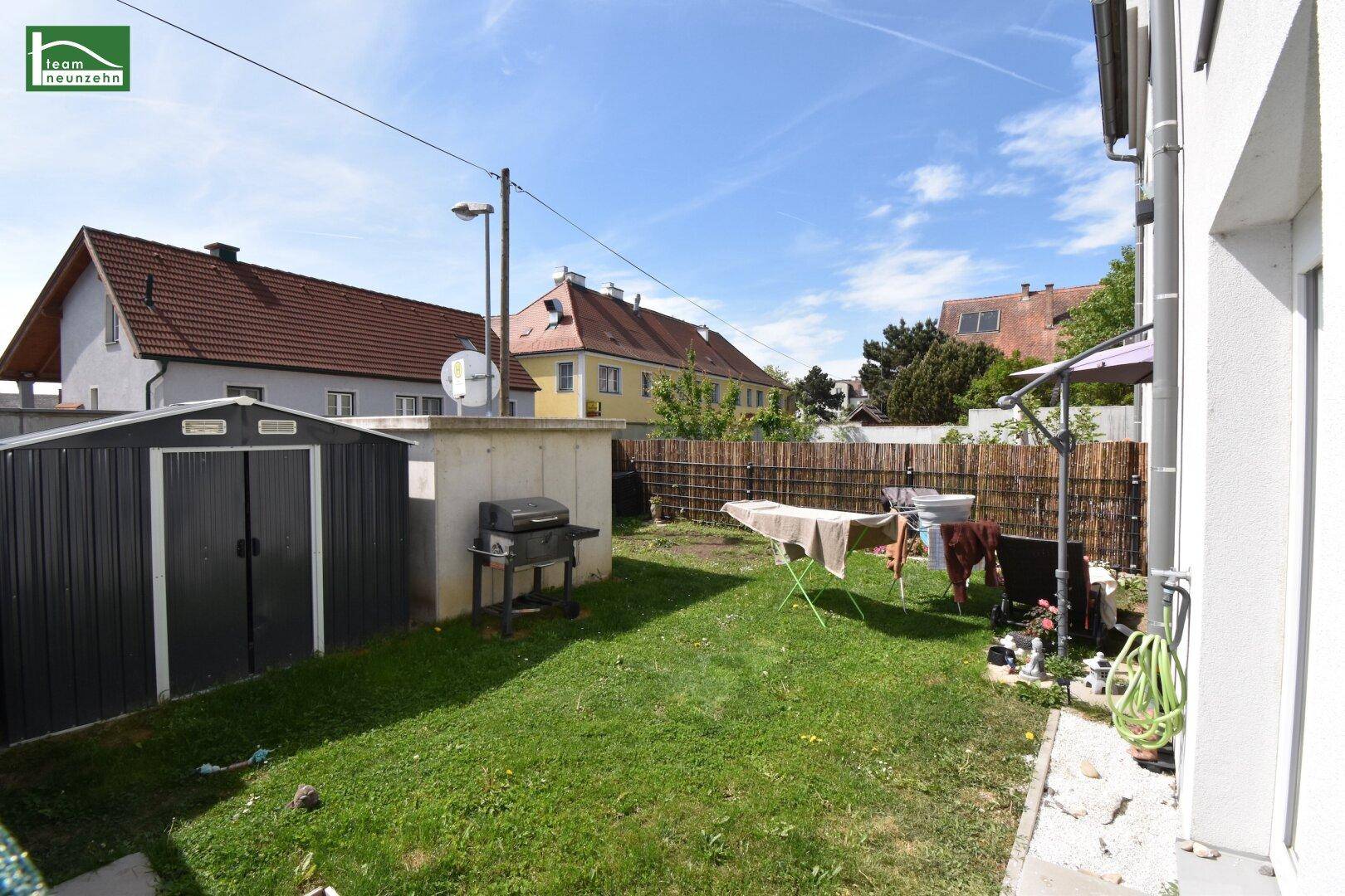 Kleiner Hinterhof mit Rasenfläche, Gartenschuppen und Grillplatz, umgeben von einem Zaun.