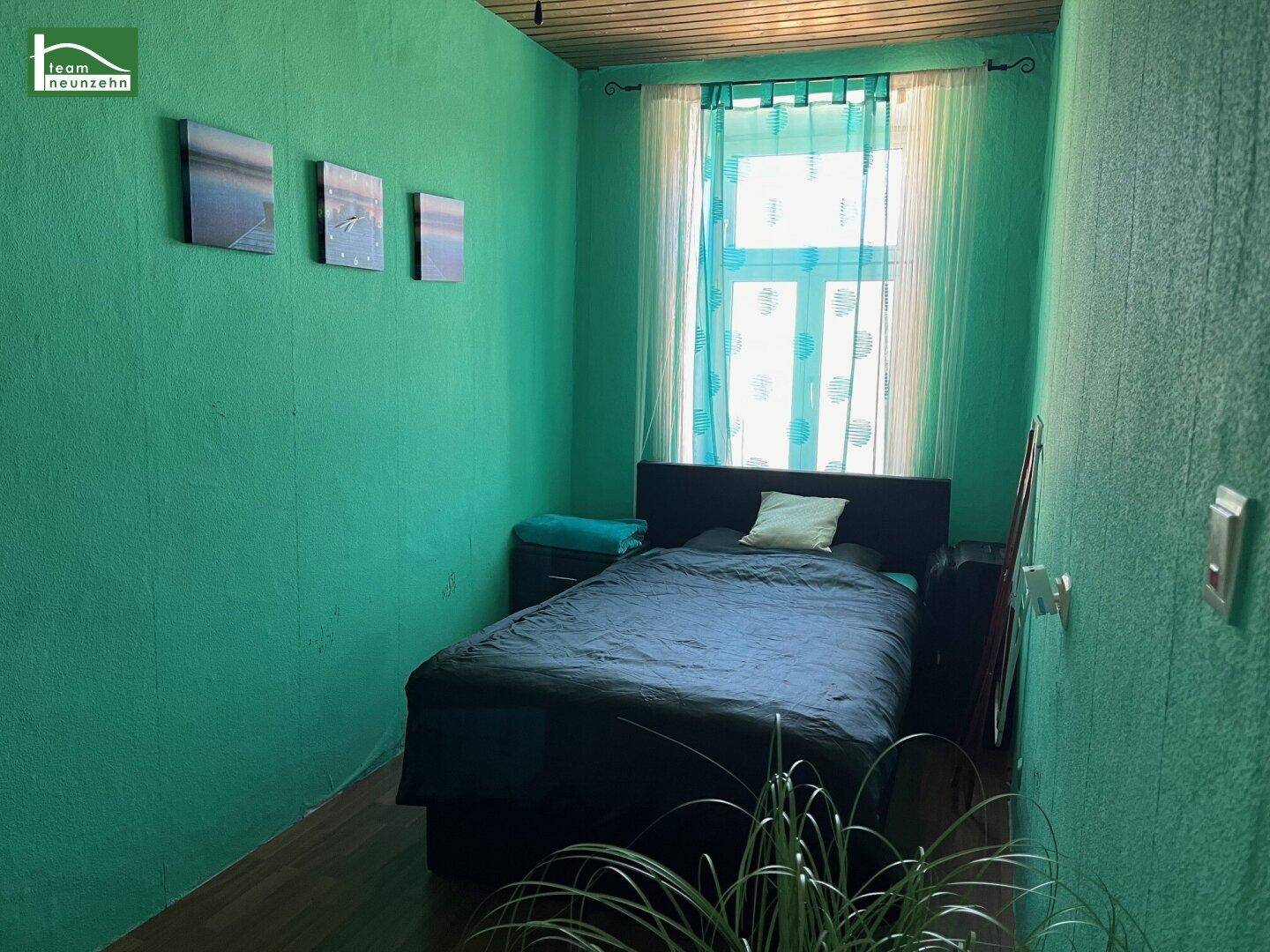 Kleines Schlafzimmer mit auffälligen grünen Wänden, einem Bett und einem Fenster mit Vorhängen.