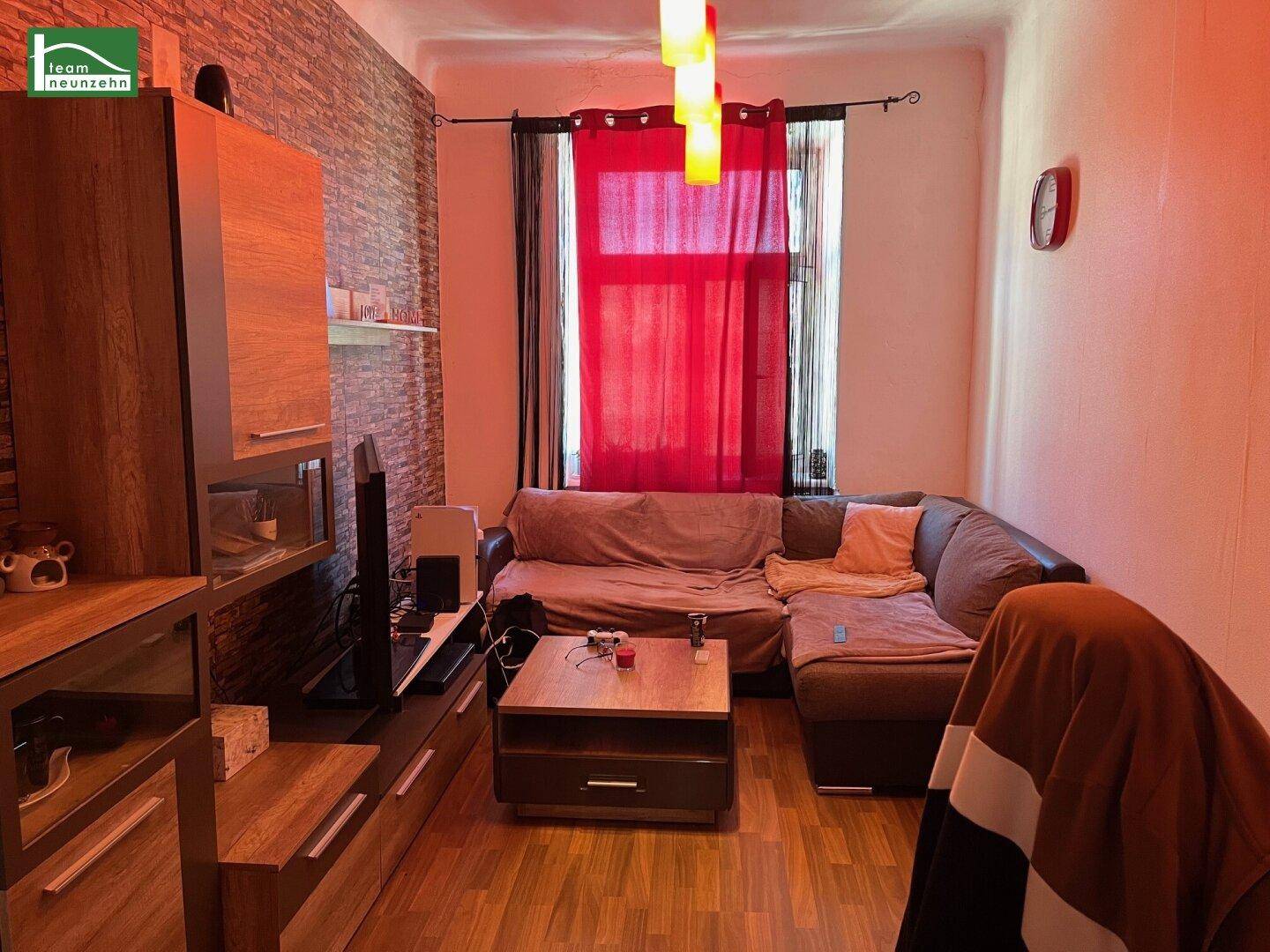 Gemütliches Wohnzimmer mit Ecksofa, TV-Möbeln und roten Vorhängen, die für Farbakzente sorgen.