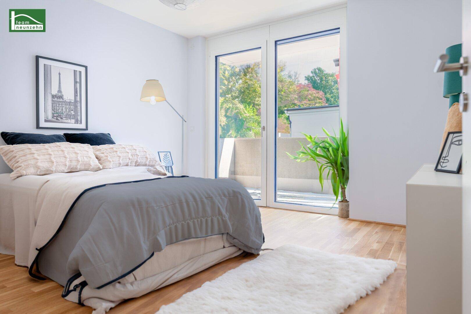 Helles Schlafzimmer mit Holzboden und großen Glastüren, die zu einem Balkon oder einer Terrasse führen.