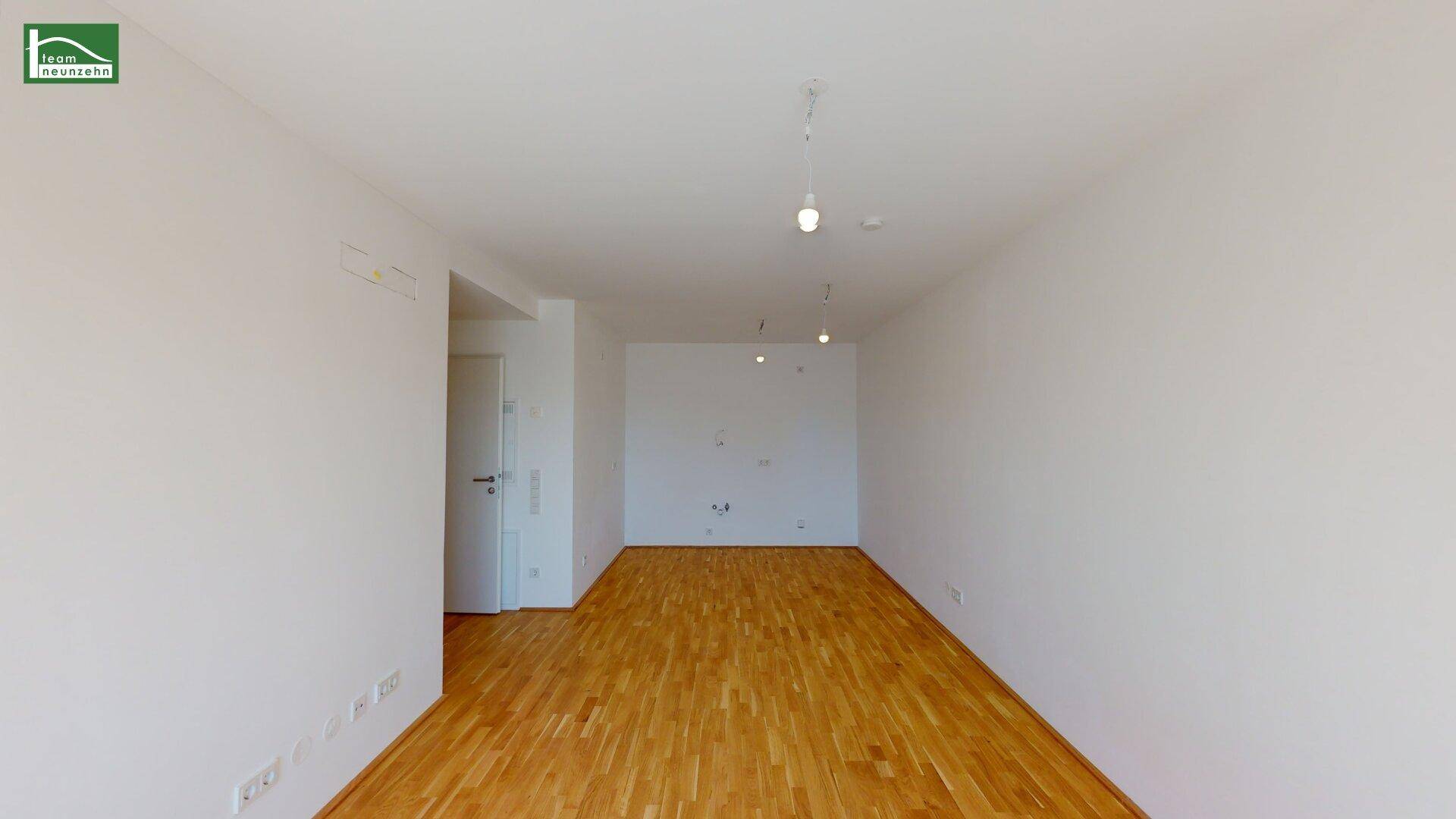 Geräumiges, leeres Wohnzimmer mit hellem Parkettboden und weißen Wänden, bereit zur Einrichtung.