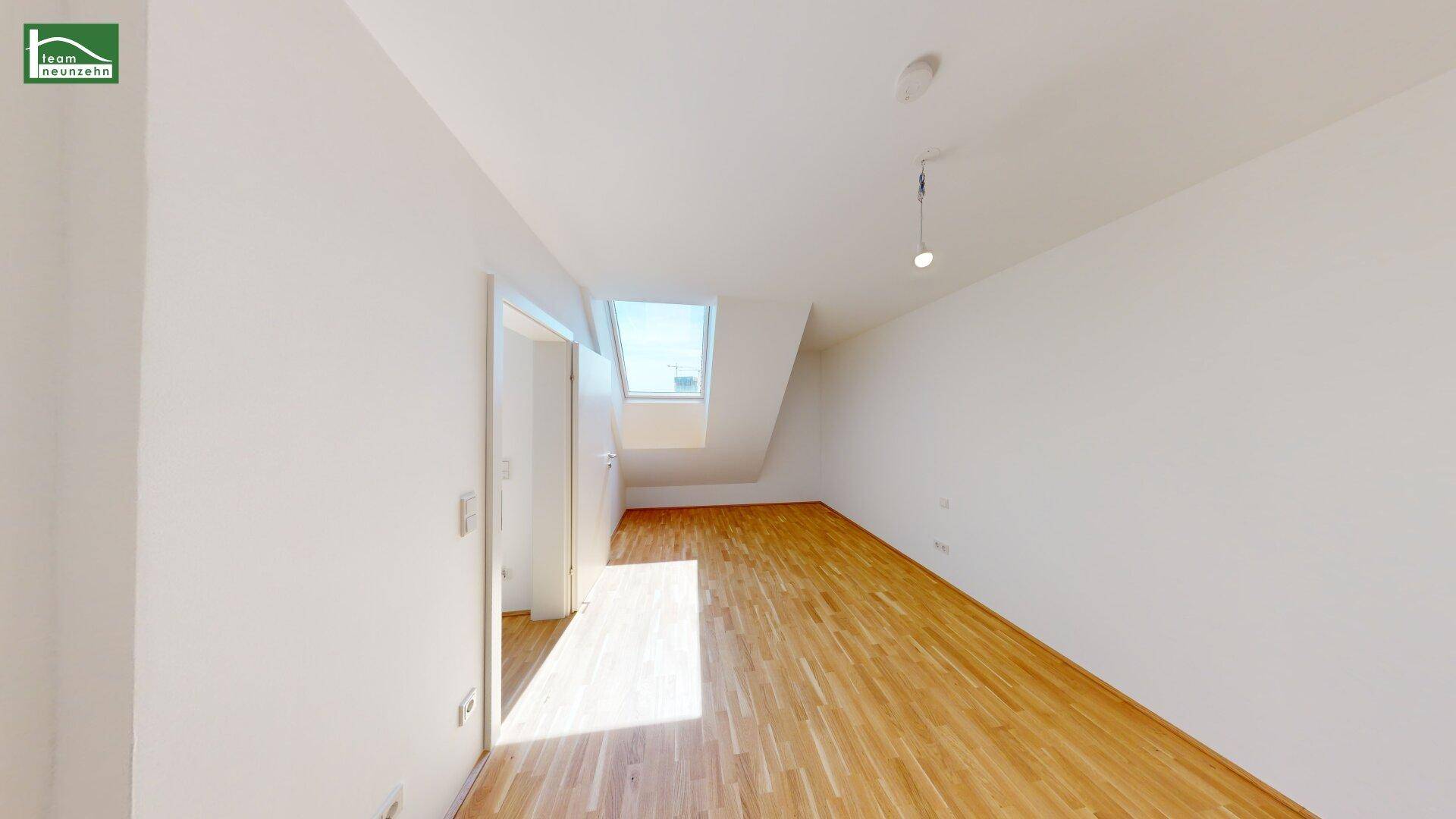 Dachgeschosszimmer mit schrägen Wänden, Dachfenster und Holzboden, bietet viel Tageslicht.