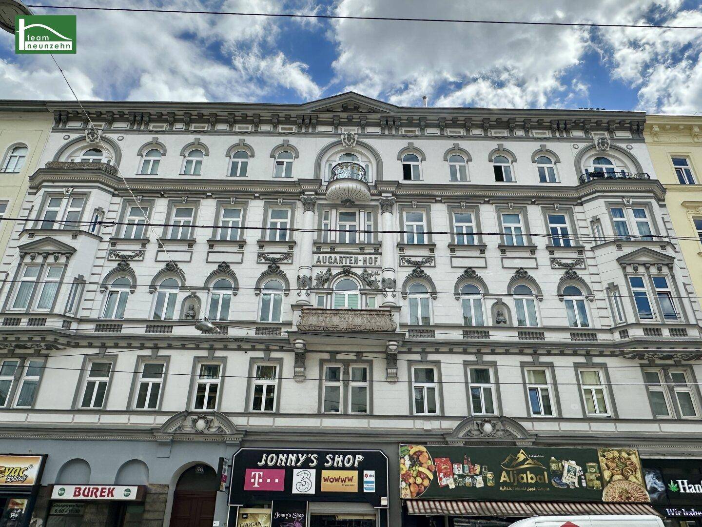 Historische Fassade des Augarten-Hofs mit klassischer Architektur und Geschäften im Erdgeschoss.