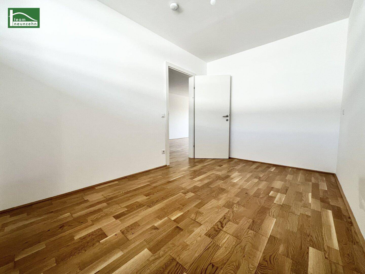 Helles, leeres Zimmer mit Parkettboden und weiß gestrichenen Wänden, bereit zur Einrichtung.