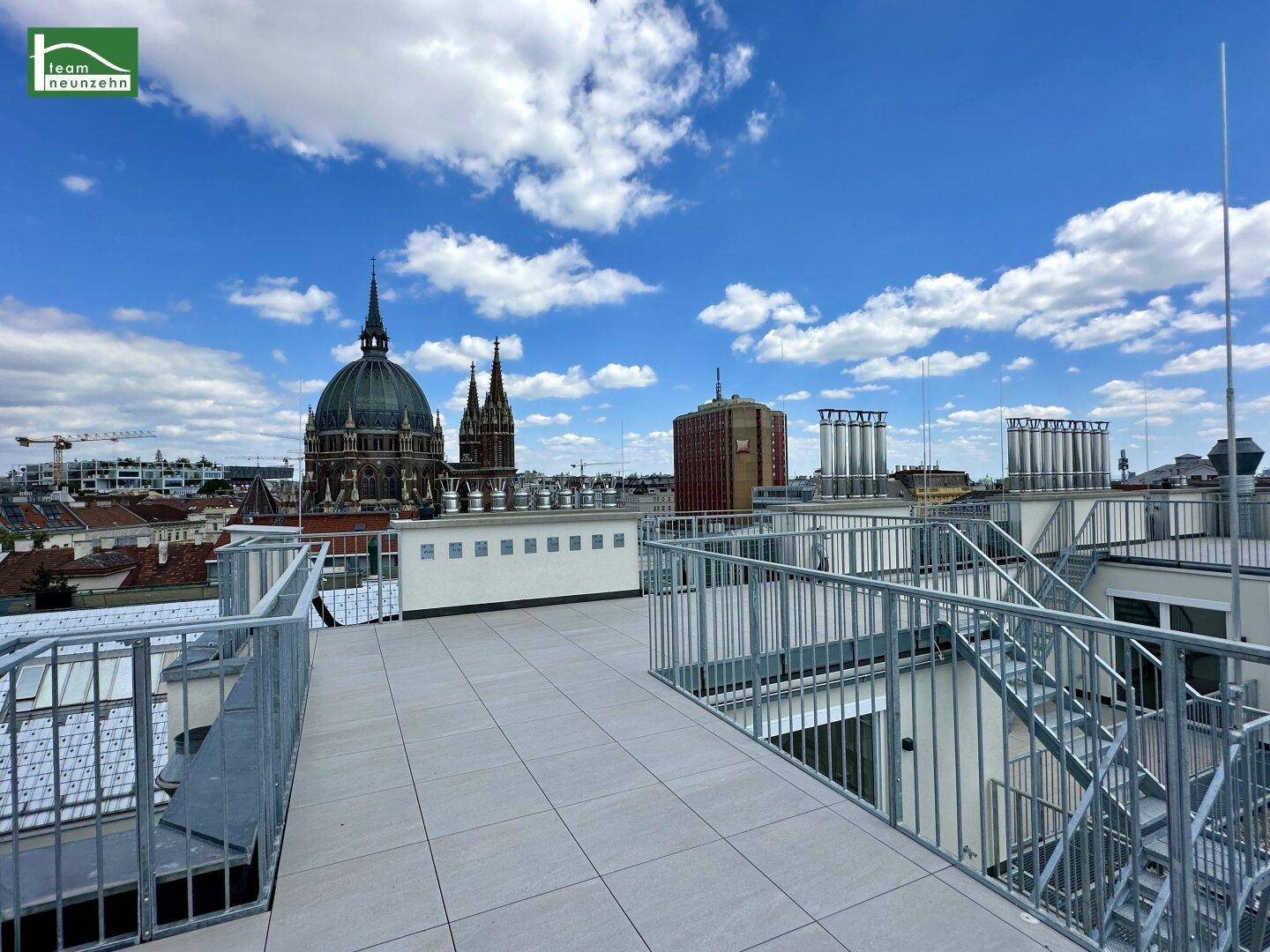 Weitläufige Dachterrasse mit Panoramablick auf die Stadt und historische Gebäude unter blauem Himmel.