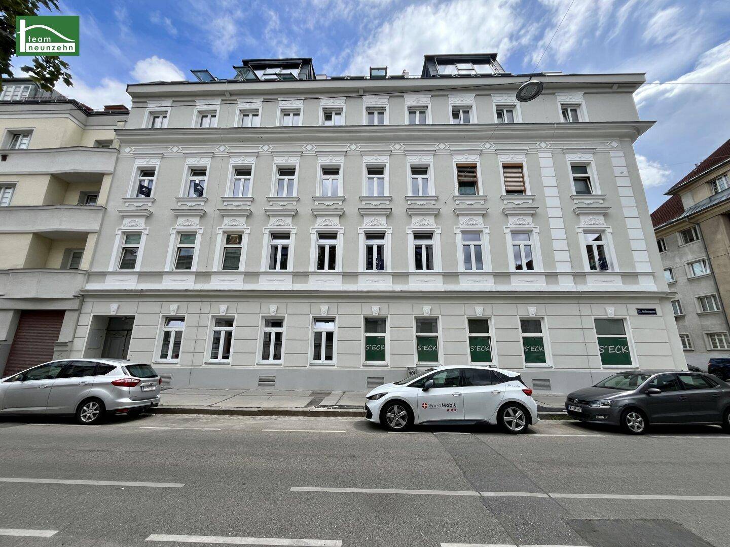Die Vorderansicht des Gebäudes zeigt eine klassische Fassade mit vielen Fenstern und Geschäften im Erdgeschoss.