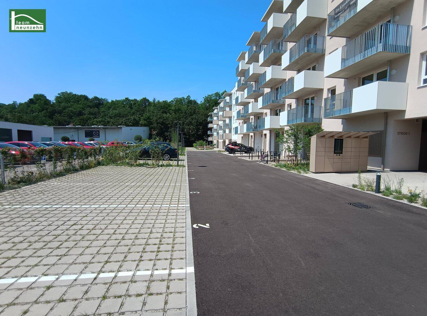 Außenansicht einer modernen Wohnanlage mit zahlreichen Parkplätzen und umgebenden Grünflächen.