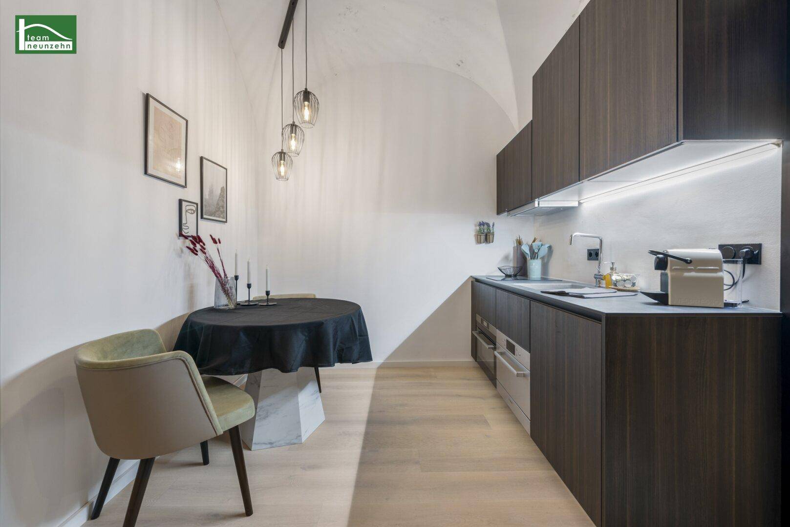 Moderne Küchenzeile mit dunklen Holzschränken und kleinem Essbereich unter gewölbter Decke.