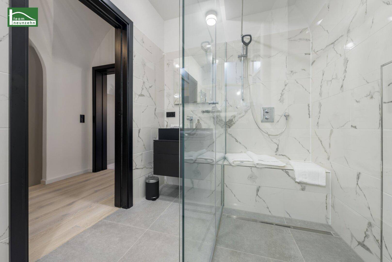 Modernes Badezimmer mit begehbarer Dusche, Marmoroptik-Fliesen und dunklem Waschtisch.