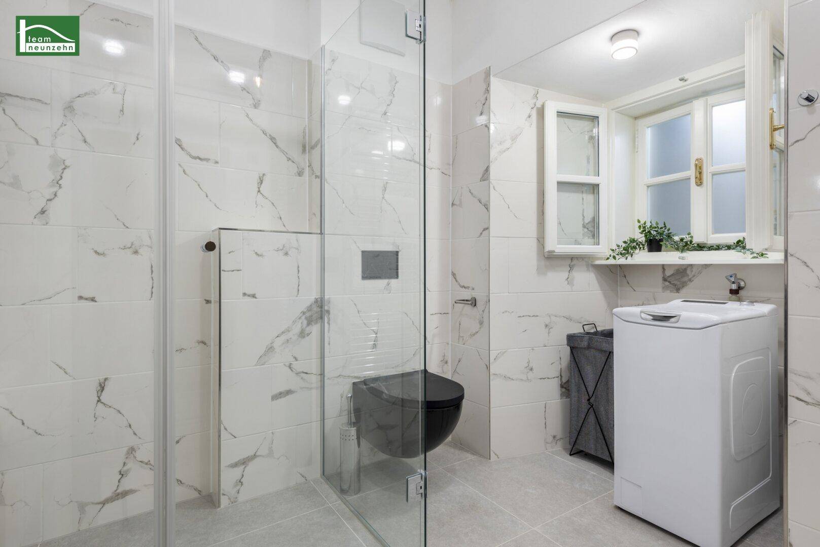 Helles Badezimmer mit Toilette, Waschmaschine und Fenster, gefliest in Marmoroptik.