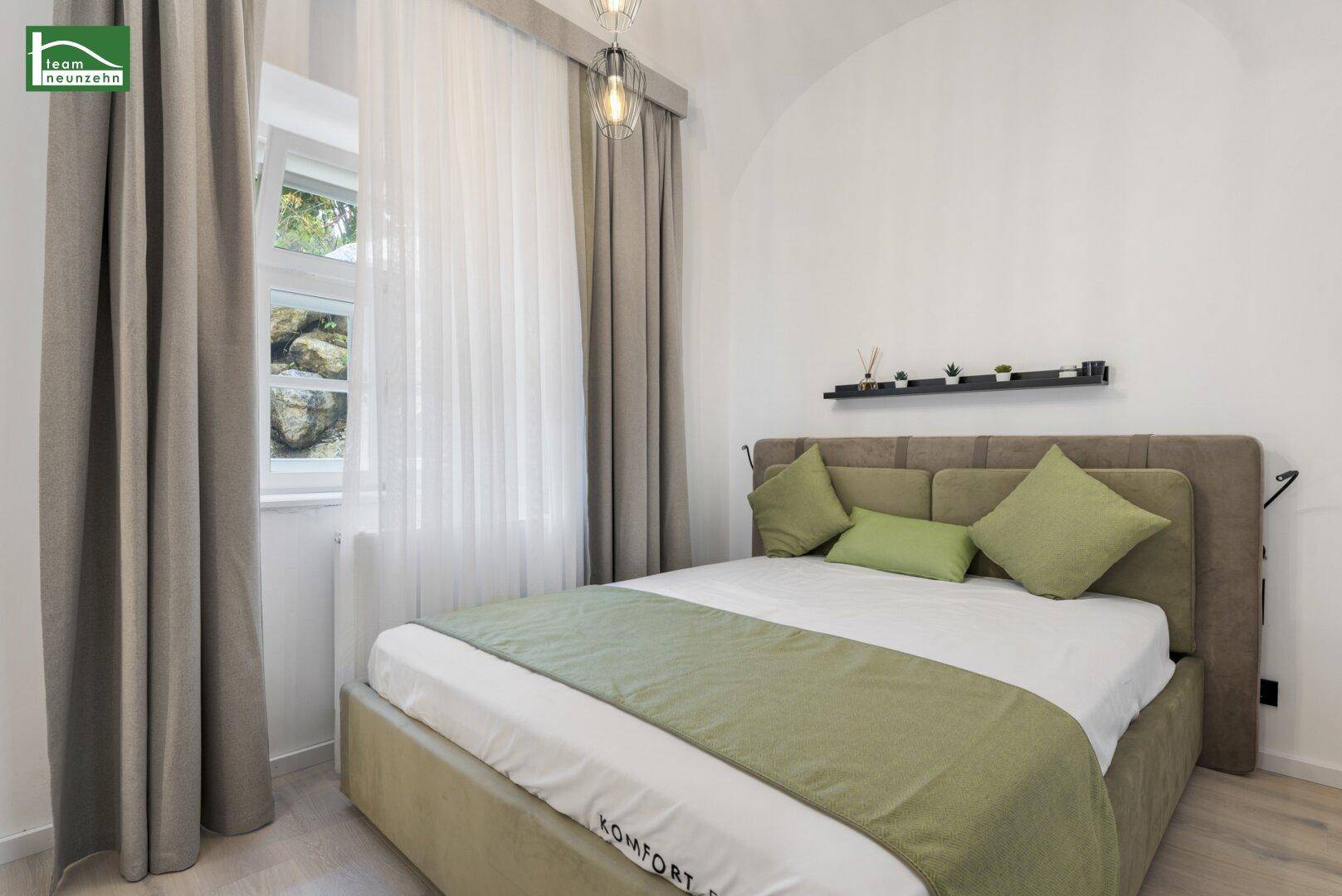 Gemütliches Schlafzimmer mit beigem Bett, grünen Kissen und gewölbter Decke, hell beleuchtet.