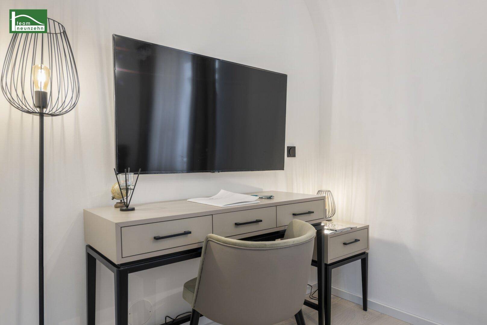Moderner Arbeitsplatz mit wandmontiertem Fernseher und stilvoller Stehlampe in hellem Raum.