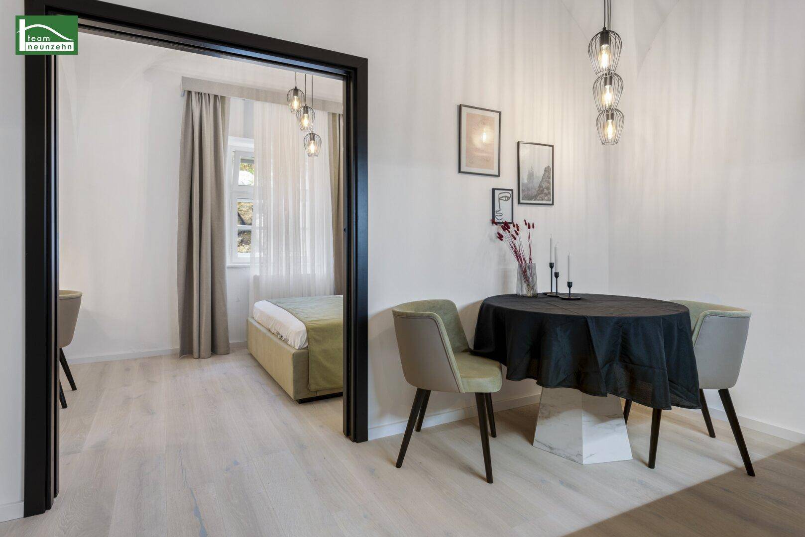 Offener Bereich mit Essplatz und Blick in das angrenzende Schlafzimmer, mit Holzboden.