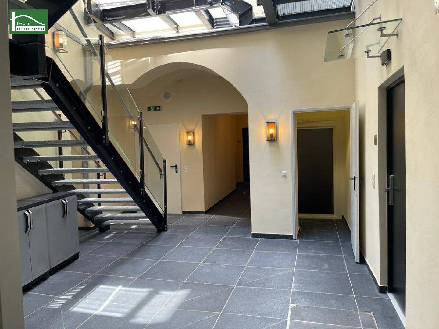 Heller Eingangsbereich mit moderner Treppe, Glasgeländer und Oberlicht für viel Tageslicht.