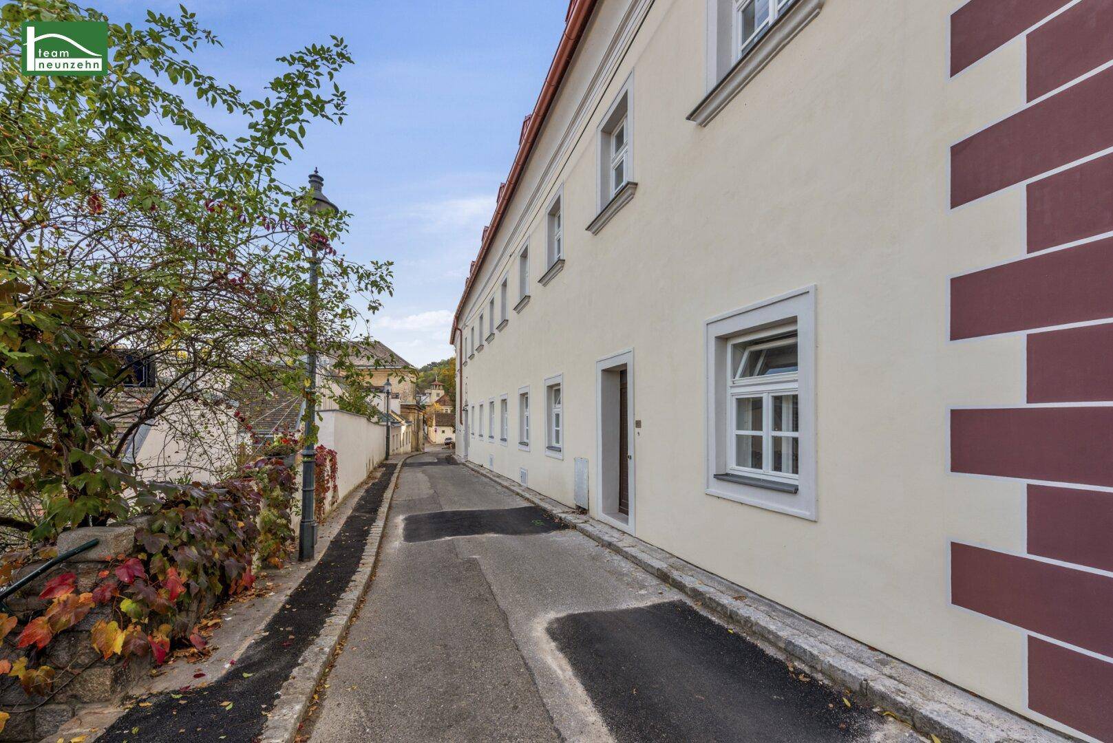 Schmale Gasse entlang der gut erhaltenen Fassade eines historischen Gebäudes mit Herbstlaub.