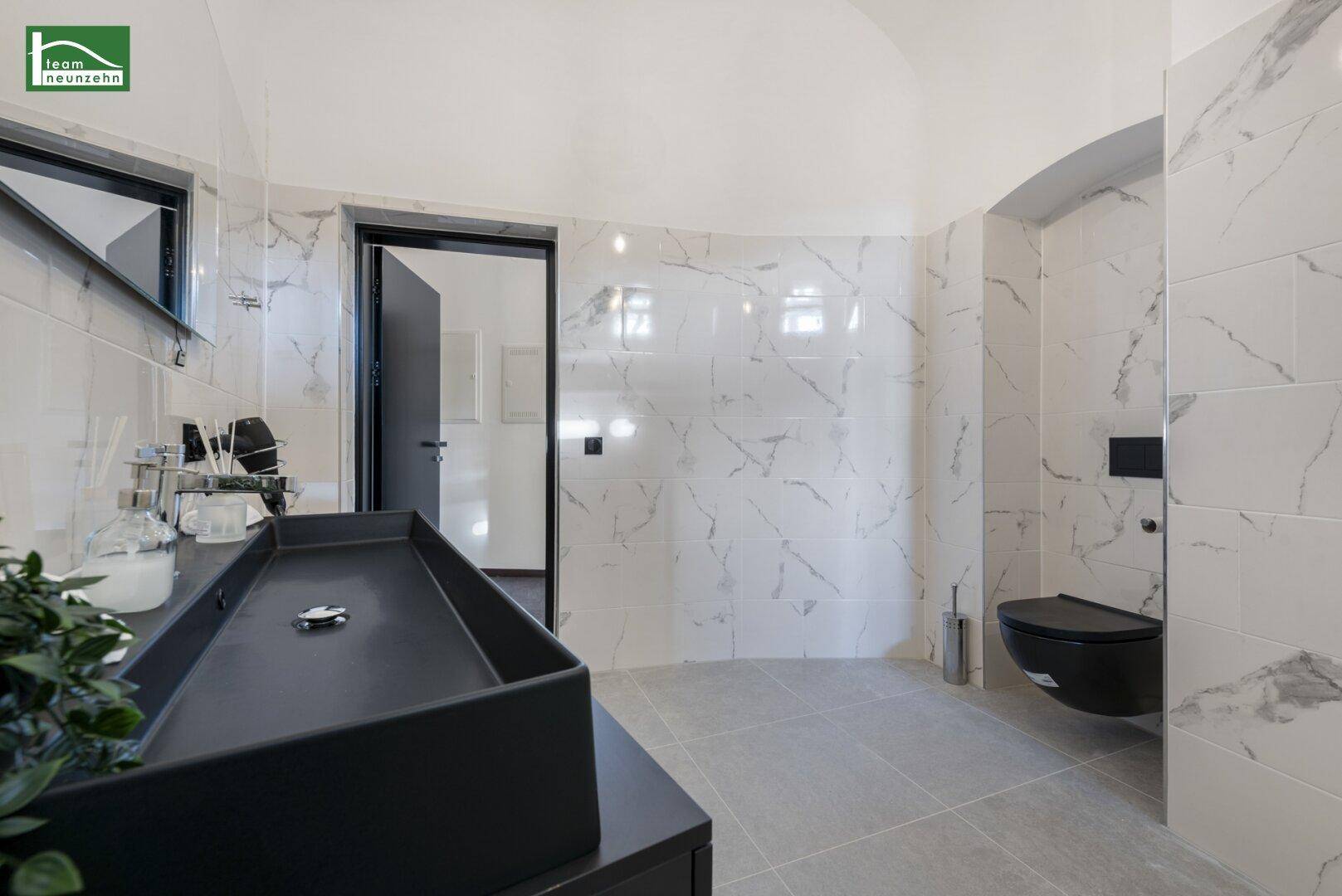 Elegantes Badezimmer mit schwarzem Waschbecken, Wandtoilette und Marmorfliesen.