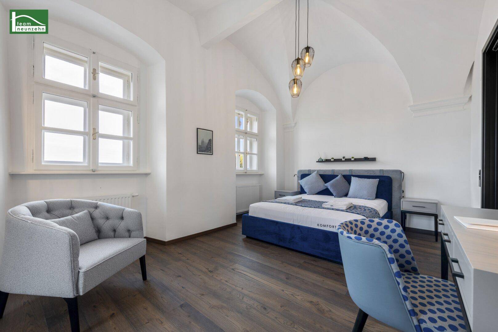 Geräumiges Schlafzimmer mit Sitzgelegenheit, Holzboden und großen Fenstern.